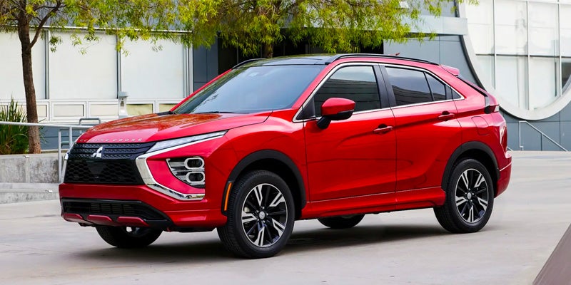 Image of a red 2024 Mitsubishi Eclipse Cross (front angle) in front of an urbanscape backdrop