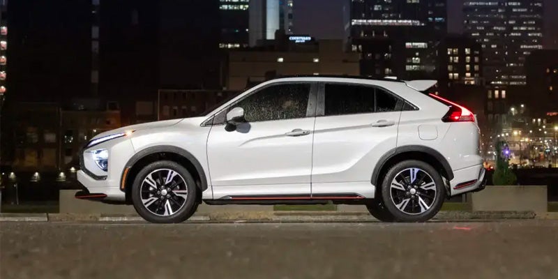 Image of a white 2024 Mitsubishi Eclipse Cross (side profile) in front of a nighttime cityscape backdrop