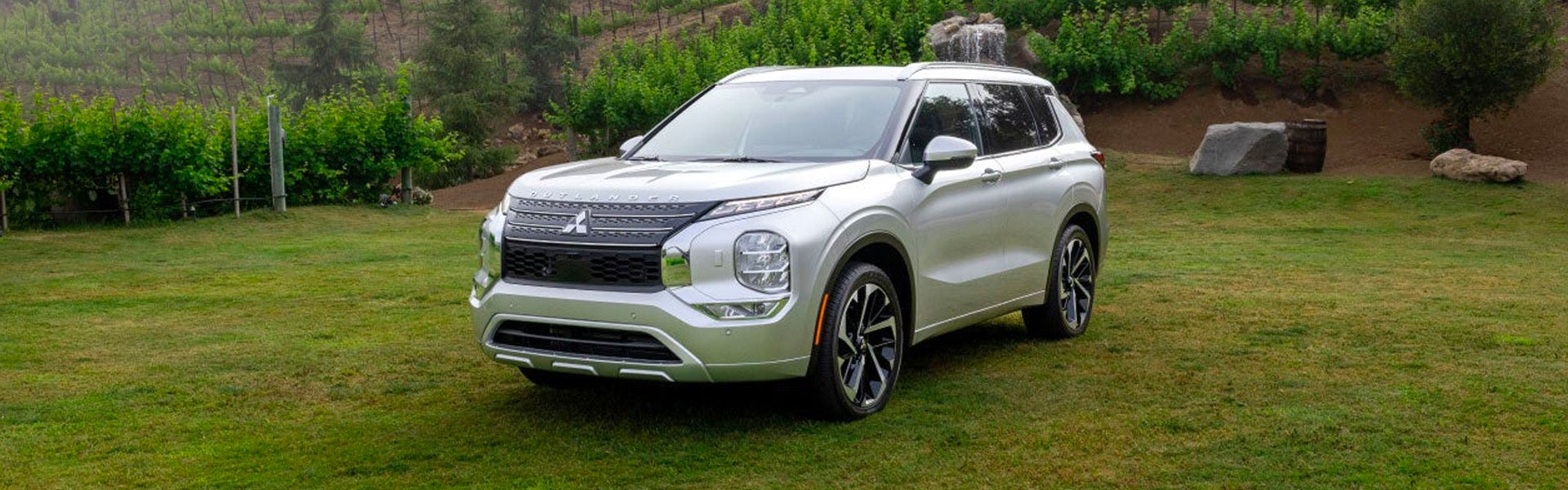 Hero image of the white 2024 Mitsubishi Outlander parked in front of a lush vineyard or garden