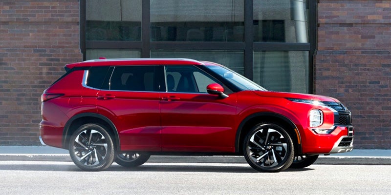 Image of the red 2024 Mitsubishi Outlander (side profile) with a brick urbanscape backdrop